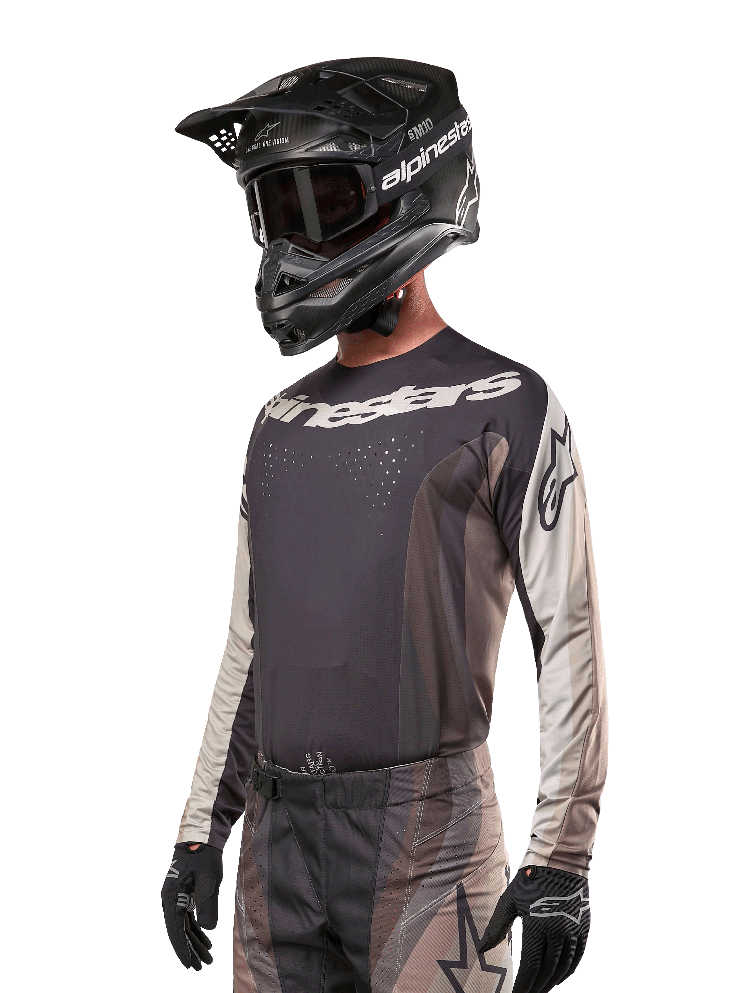 Maillot Alpinestars Techstar Pneuma 2024, maillot de motocross, sable foncé et gris fer, haut de performance à manches longues avec perforations au laser et logos blancs, porté avec un pantalon assorti et un casque noir, coupe athlétique pour le pilotage tout-terrain