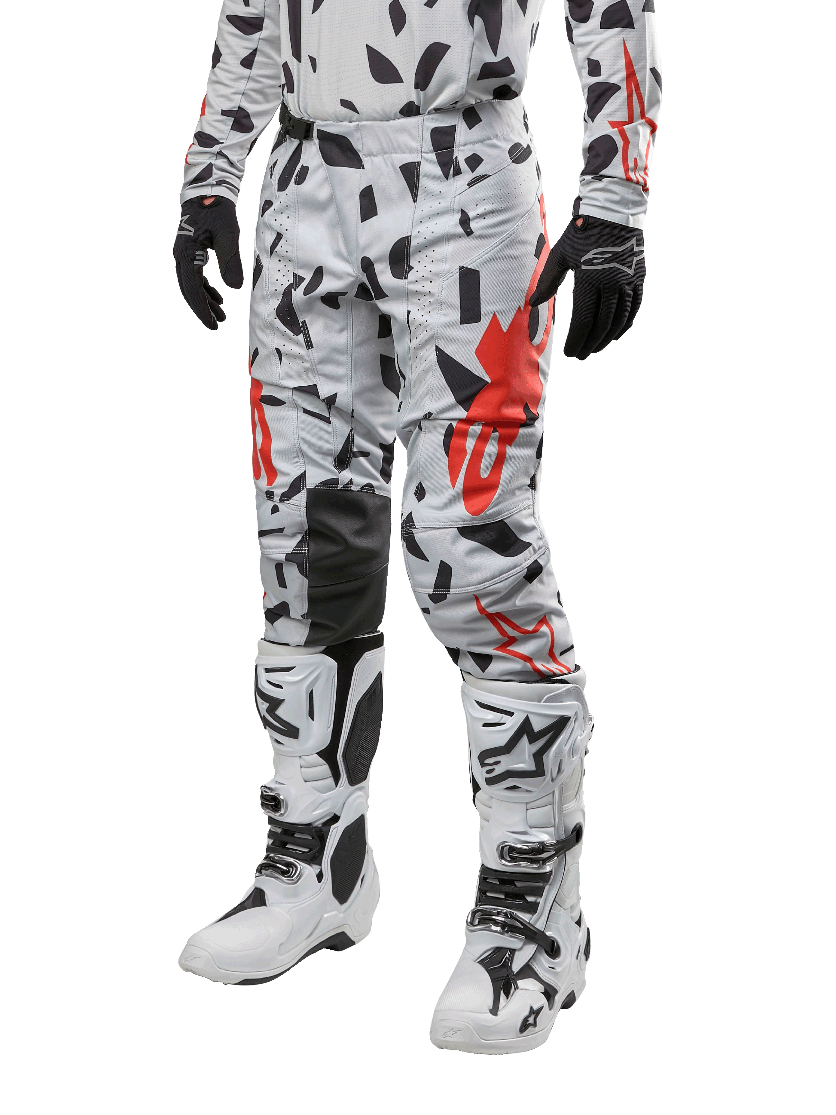 Alpinestars Pantalon Techstar Rantera 2024, pantalon de motocross, camouflage gris brume avec motifs abstraits noirs et rouges, porté avec un maillot assorti, des gants noirs et des bottes de motocross blanches, conçu pour la course tout-terrain haute performance