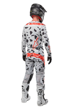 Motocross rider from the back wearing Alpinestars 2024 Techstar Rantera Pants, Haze Gray Camo with black spots and red logos, matching jersey, black helmet, and white boots, complete off-road racing outfit