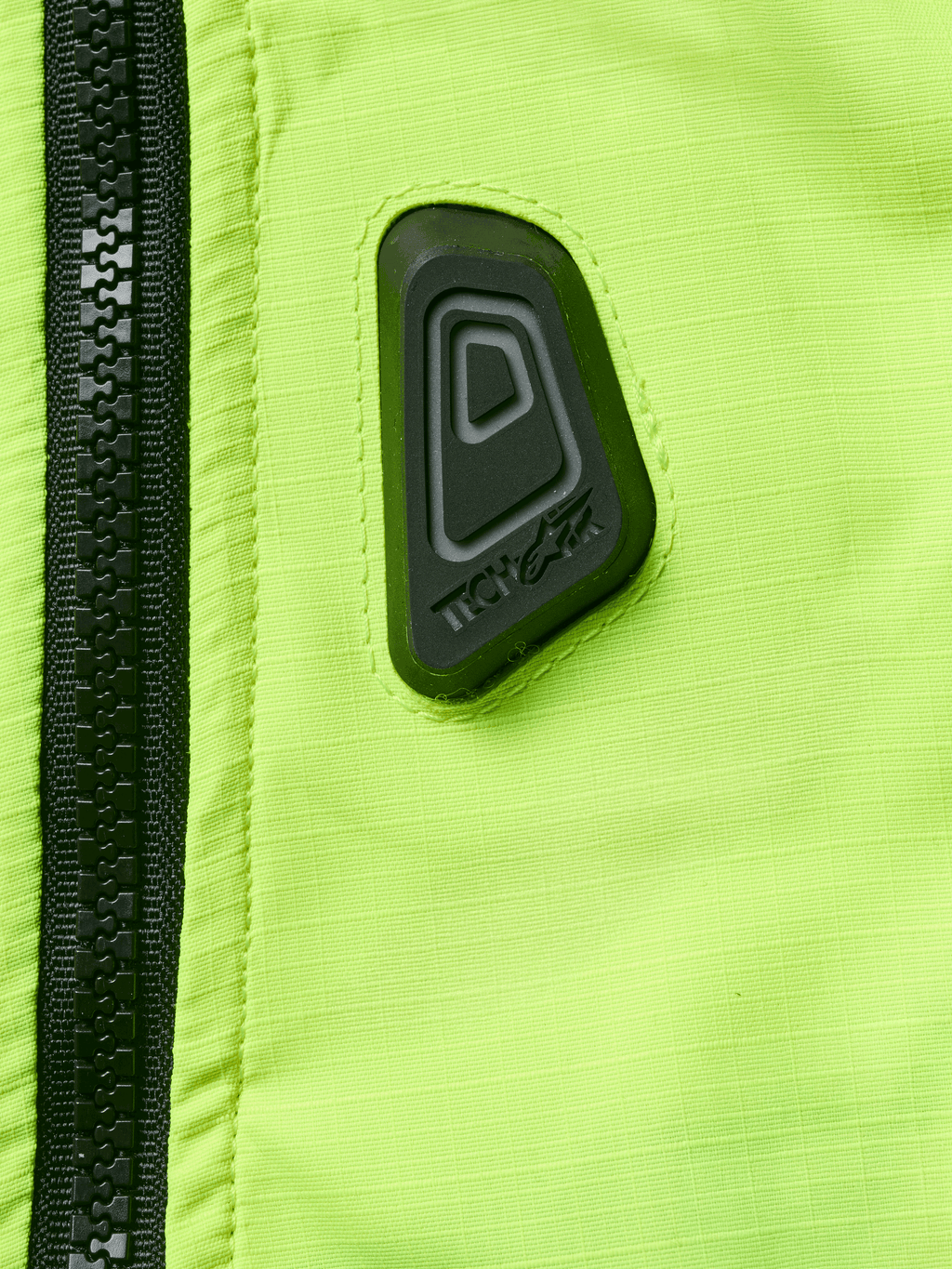 Alpinestars Tech-Air® 3 V2 System, gilet airbag moto, gros plan sur le tissu jaune fluo résistant à l'eau avec fermeture éclair noire, logo Tech-Air en caoutchouc noir, équipement de sécurité haute visibilité