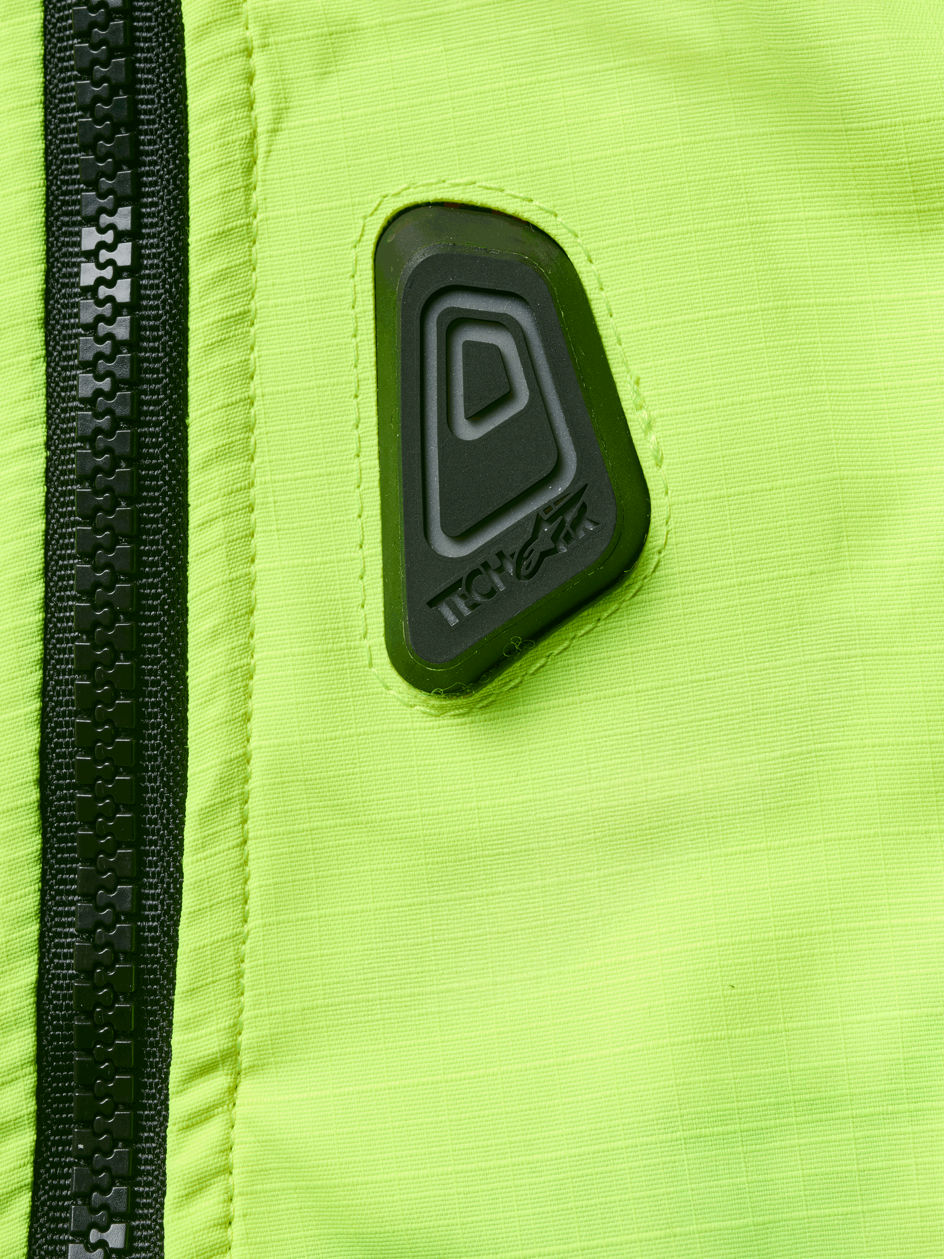 Alpinestars Tech-Air® 3 V2 System, gilet airbag moto, gros plan sur le tissu jaune fluo résistant à l'eau avec fermeture éclair noire, logo Tech-Air en caoutchouc noir, équipement de sécurité haute visibilité