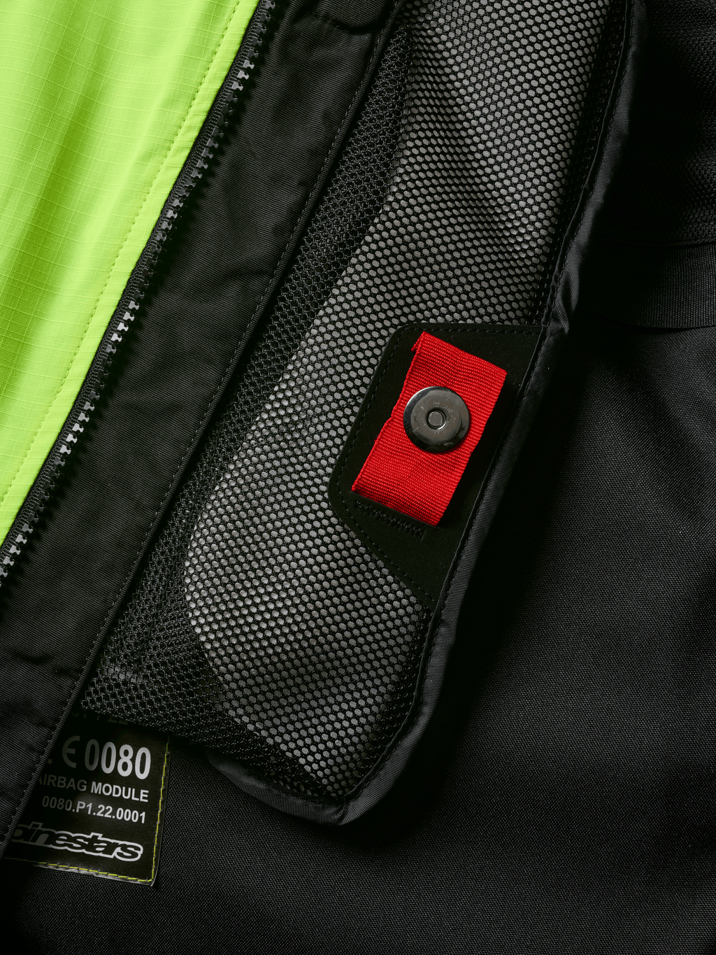 Détail du système Alpinestars Tech-Air® 3 V2, gros plan sur la poche intérieure en filet avec tirette rouge et bouton-pression, empiècement jaune fluo, construction textile noire montrant l'étiquette du module d'airbag et la fermeture éclair