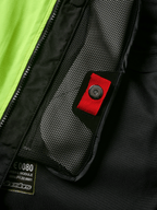 Détail du système Alpinestars Tech-Air® 3 V2, gros plan sur la poche intérieure en filet avec tirette rouge et bouton-pression, empiècement jaune fluo, construction textile noire montrant l'étiquette du module d'airbag et la fermeture éclair