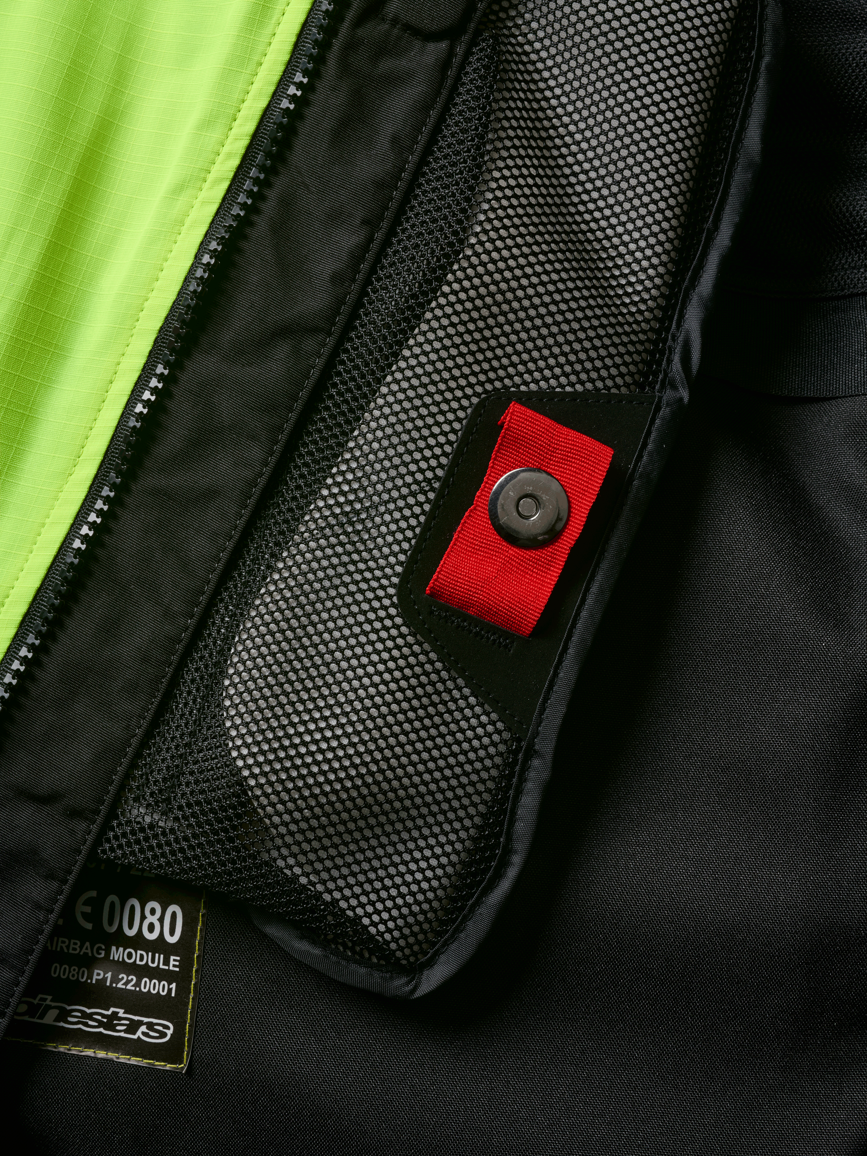 Détail du système Alpinestars Tech-Air® 3 V2, gros plan sur la poche intérieure en filet avec tirette rouge et bouton-pression, empiècement jaune fluo, construction textile noire montrant l'étiquette du module d'airbag et la fermeture éclair