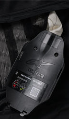 Alpinestars Tech-Air 3 V2 System, vue interne de l'inflateur de gaz et du boîtier de l'ECU, plastique noir avec logo embossé, étiquette de sécurité avec code QR et schémas d'installation, doublure intérieure en mesh noir, détail du système d'airbag autonome réparable par l'utilisateur