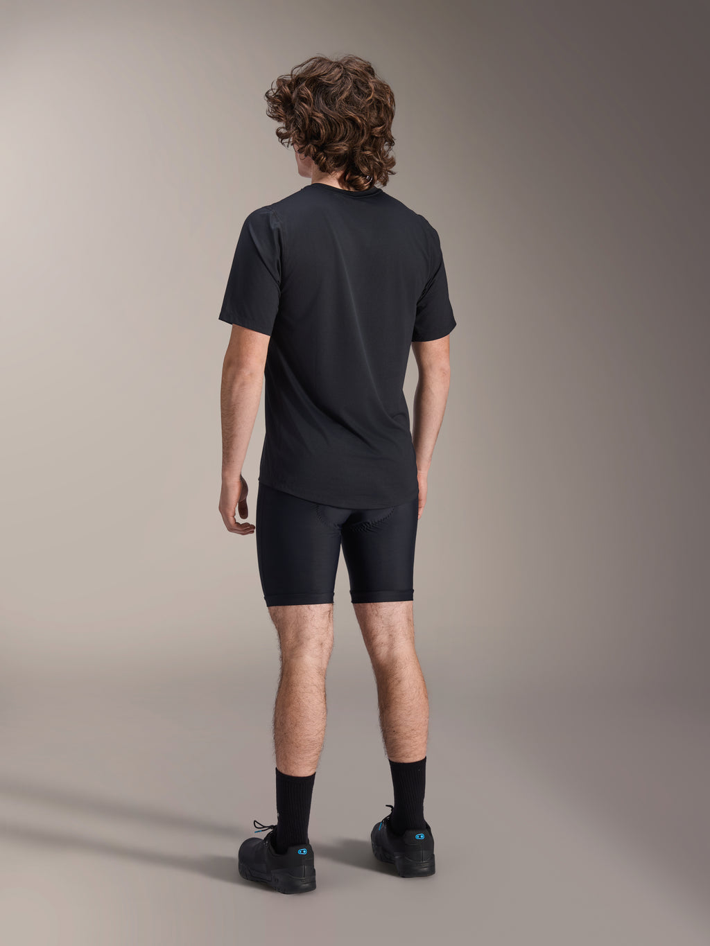 Alpinestars A-Dura Liner Shorts, short de cyclisme noir, vue de dos sur modèle, tissu extensible ajusté avec coutures de rembourrage de chamois visibles, associé à un t-shirt noir et des chaussures de cyclisme, équipement de VTT