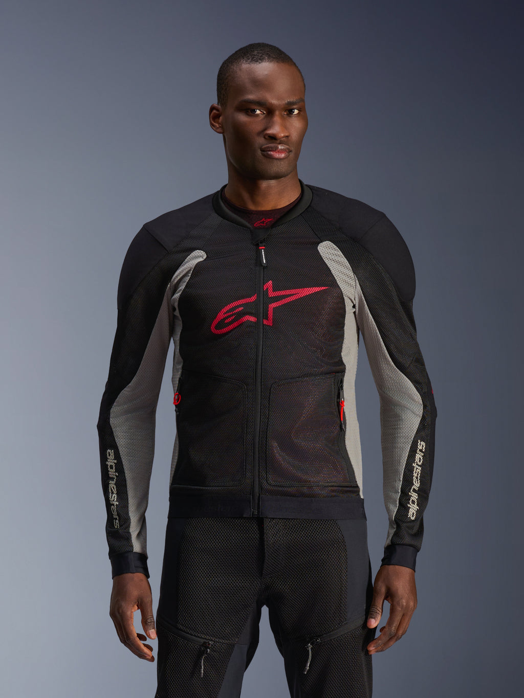 Alpinestars Troop-Air Jacket, veste de moto en mesh, noir et gris cendré avec accents rouge vif, portée par un mannequin, dotée de panneaux en mesh technique 2D respirants pour la ventilation, grand logo Astars rouge sur la poitrine, design technique et sportif pour la conduite urbaine