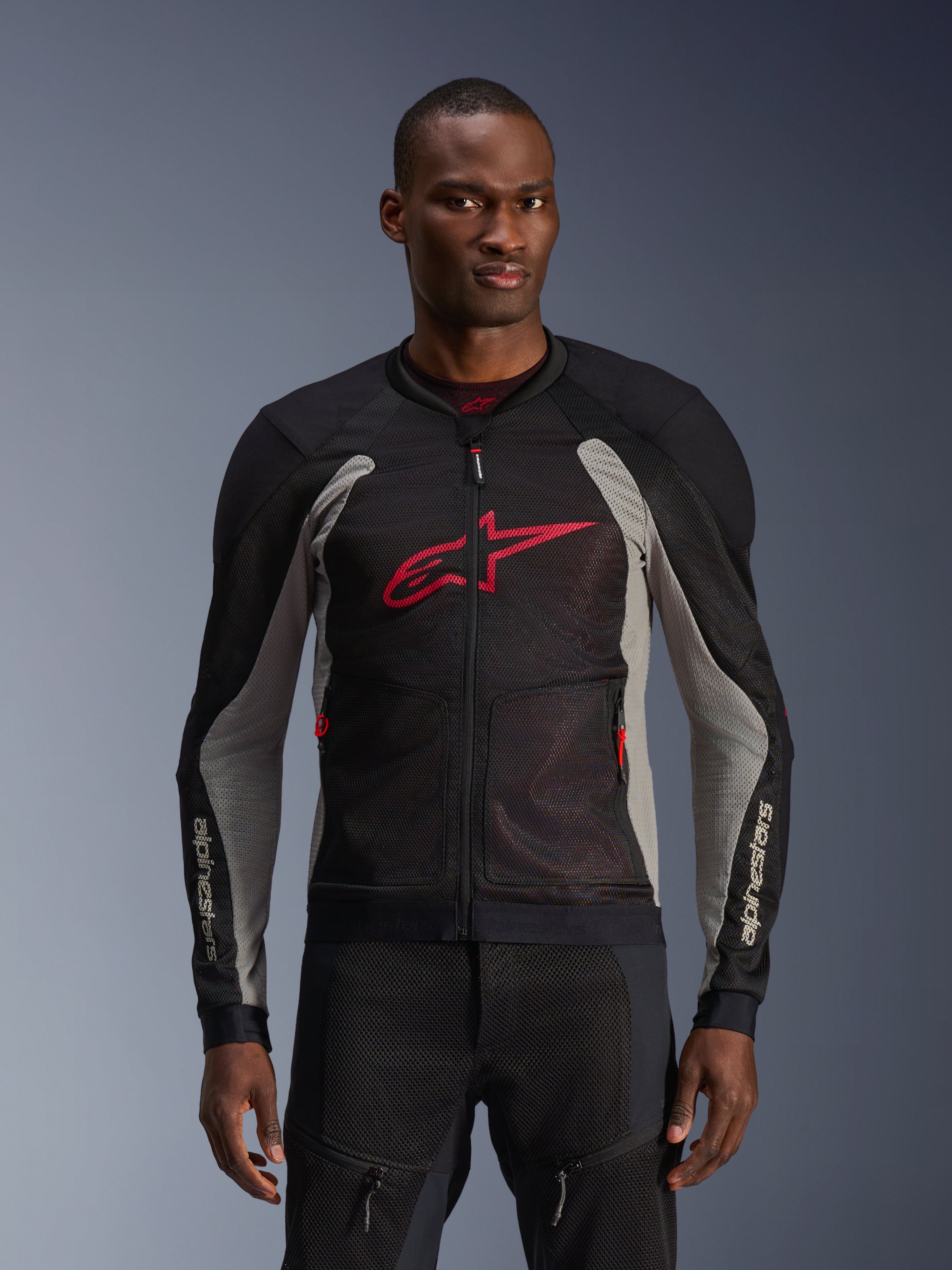 Alpinestars Troop-Air Jacket, veste de moto en mesh, noir et gris cendré avec accents rouge vif, portée par un mannequin, dotée de panneaux en mesh technique 2D respirants pour la ventilation, grand logo Astars rouge sur la poitrine, design technique et sportif pour la conduite urbaine