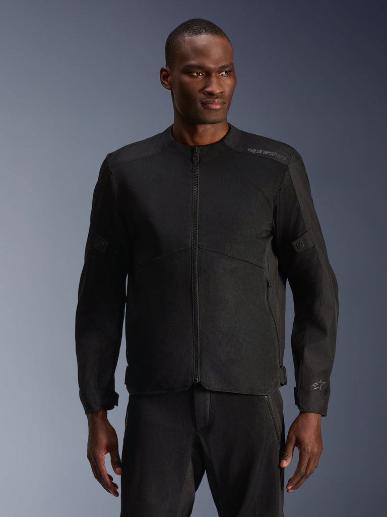 Mannequin homme portant la veste Alpinestars C-1 Air noire, une veste de moto contemporaine dotée de larges panneaux en maille technique et d'une fermeture éclair frontale intégrale, associée à un pantalon de moto noir assorti, esthétique urbaine et trajets quotidiens