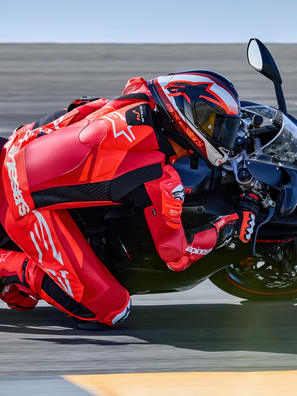Combinaison en cuir Alpinestars GP Plus V4 Sprint 1 pièce, rouge fluo et blanche, prête pour Tech-Air®, sur un pilote en plein virage sur circuit.