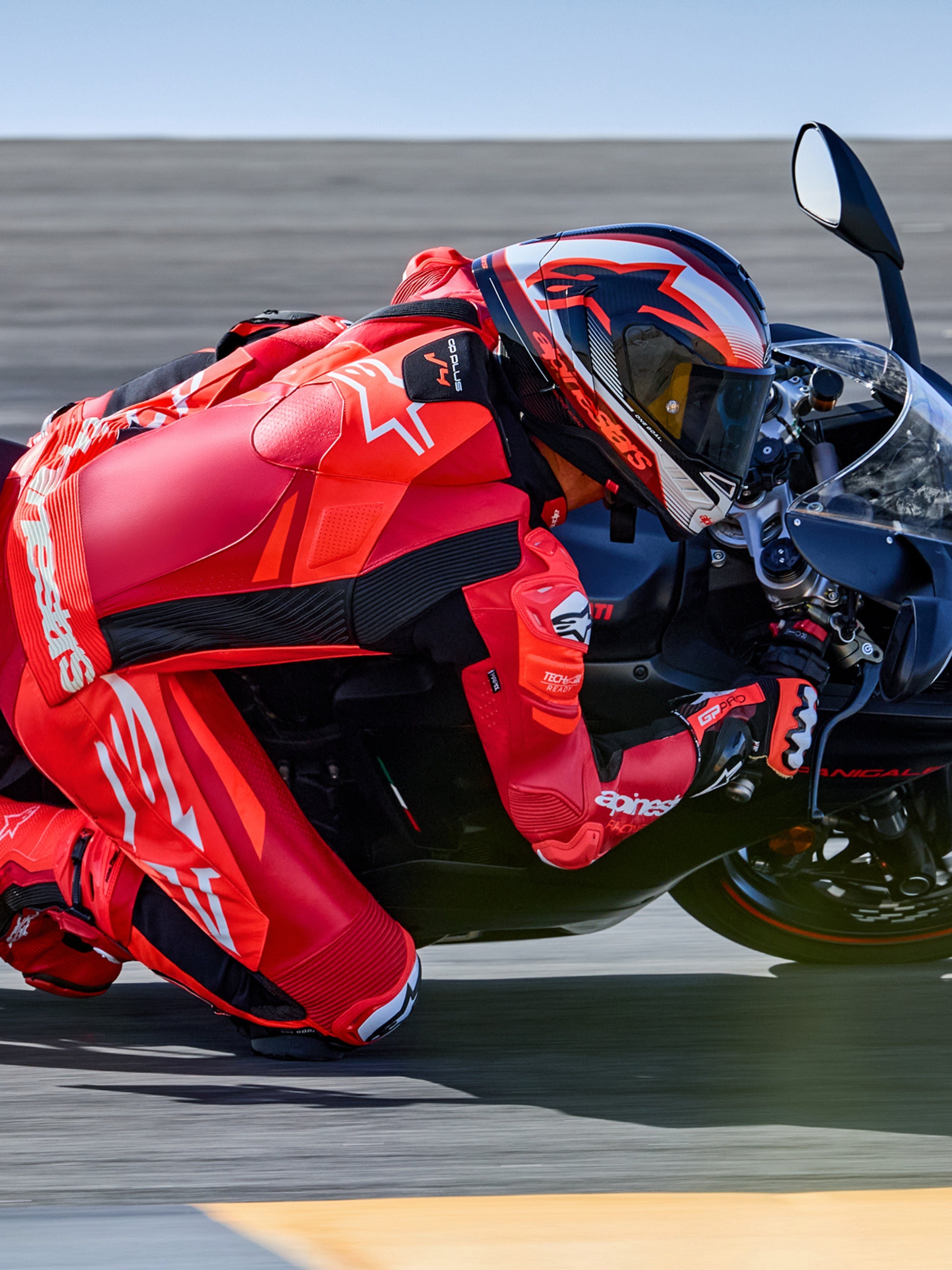 Combinaison en cuir Alpinestars GP Plus V4 Sprint 1 pièce, rouge fluo et blanche, prête pour Tech-Air®, sur un pilote en plein virage sur circuit.
