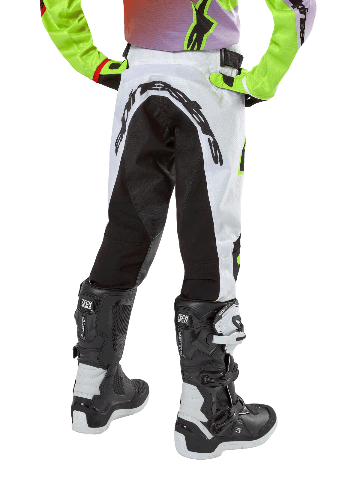 Pantalon Alpinestars Racer Lucent Junior 2024, pantalon de motocross, blanc et noir avec accents néon, vue arrière montrant le grand panneau extensible et le logo Alpinestars, porté avec des bottes Alpinestars Tech Series noires et blanches.