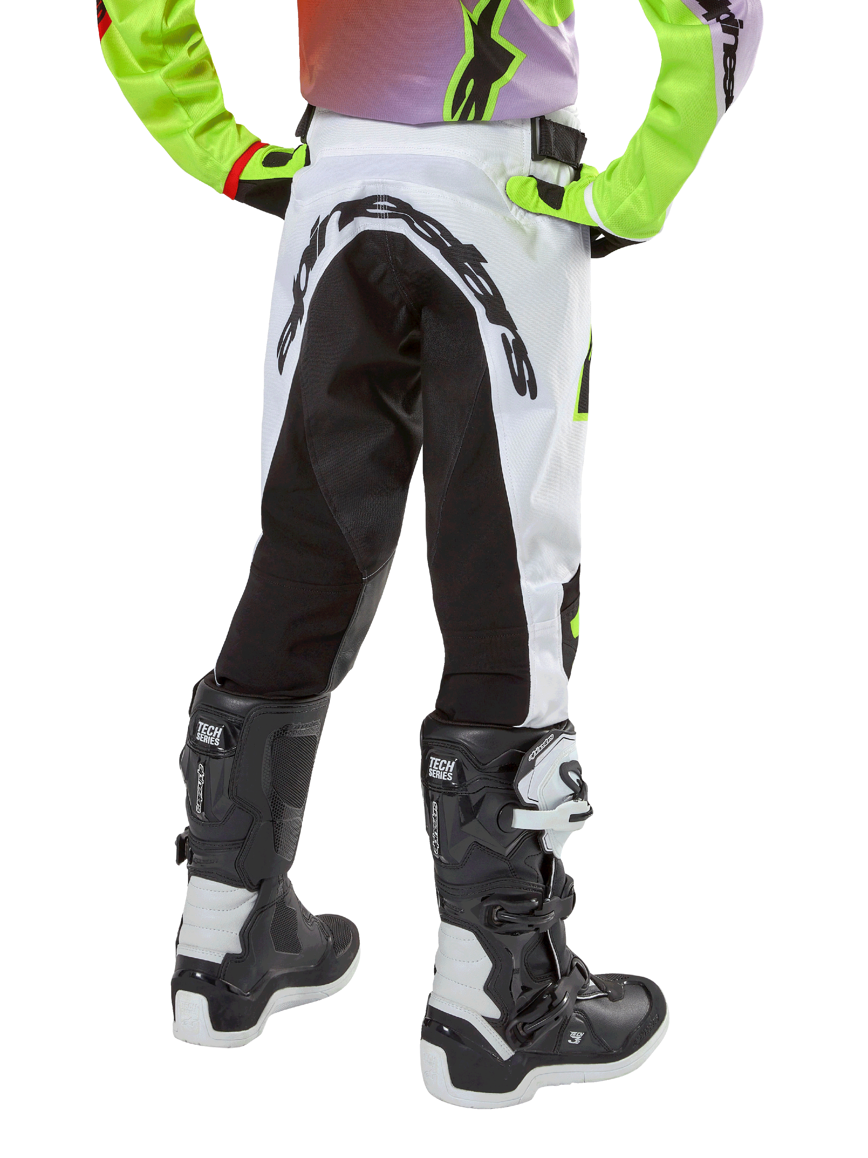 Pantalon Alpinestars Racer Lucent Junior 2024, pantalon de motocross, blanc et noir avec accents néon, vue arrière montrant le grand panneau extensible et le logo Alpinestars, porté avec des bottes Alpinestars Tech Series noires et blanches.