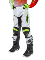 Alpinestars Youth 2024 Racer Lucent Pants, pantalon de motocross pour enfant, blanc, rouge néon et jaune fluo, vue du bas du corps avec panneaux extensibles noirs et accents néon, porté avec des bottes de course noires et blanches et des gants jaune néon, équipement technique tout-terrain pour enfant
