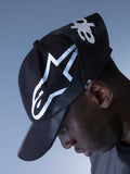 Alpinestars RSRV Resurgence Hat, casquette noire avec logo blanc audacieux, portée par une personne, design streetwear premium
