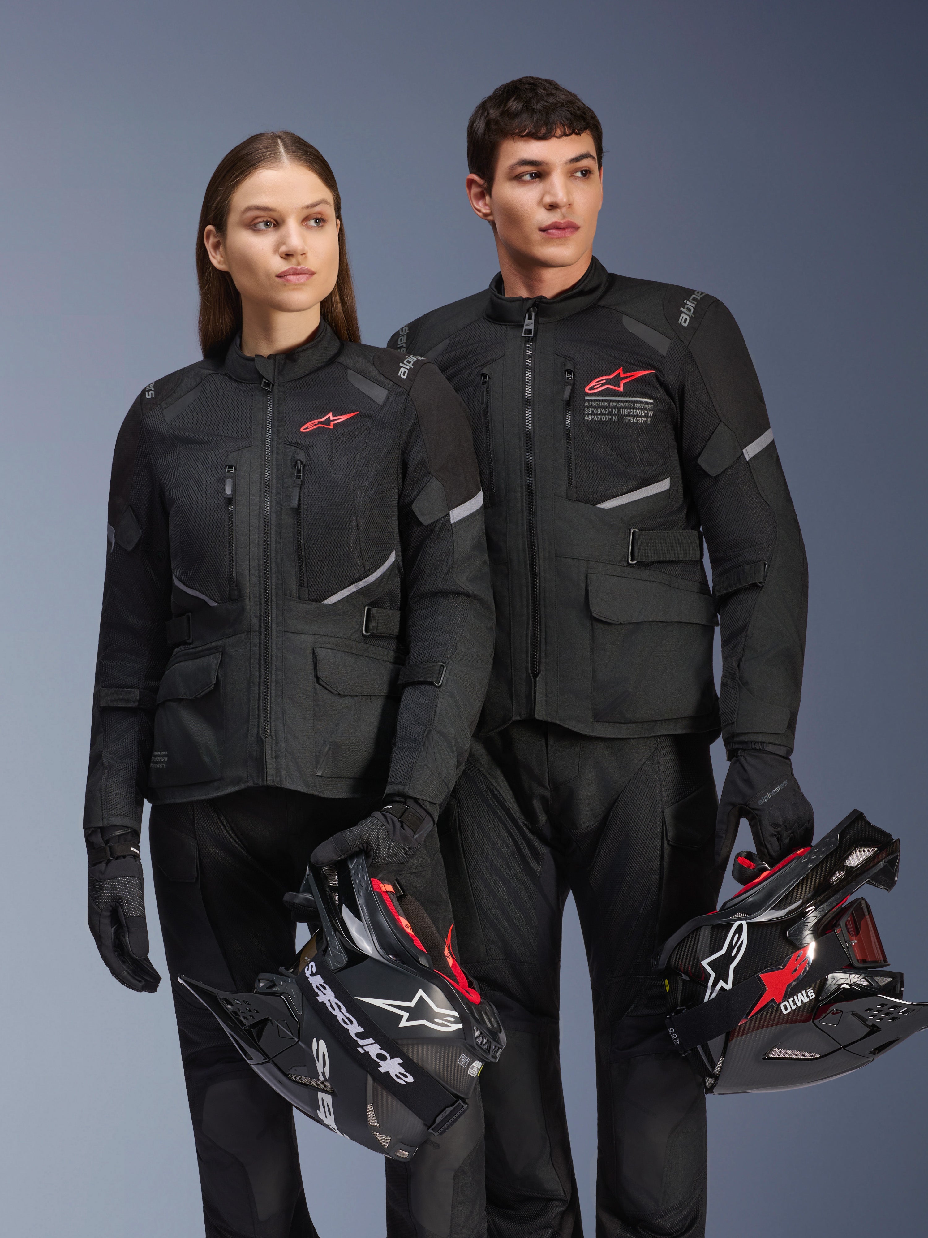 Homme et femme portant des vestes Alpinestars Andes Air Drystar®, équipement de touring aventure noir avec panneaux en mesh et détails réfléchissants, pantalons et gants noirs assortis, tenant des casques de motocross, photo de studio de vêtements de moto professionnels